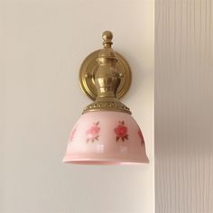 a pink and gold light hanging from the side of a white wall with flowers on it