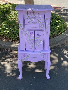 a purple dresser with flowers painted on the front and sides, next to a tree