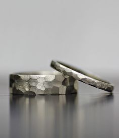 two wedding rings sitting on top of a silver table next to each other, one has a diamond pattern in the middle