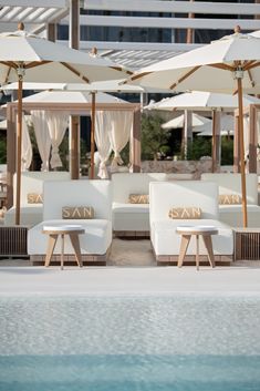 some chairs and umbrellas by the pool in front of a building with white curtains