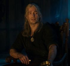 a man with long hair sitting in a chair next to a bowl and candle holder