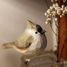 a small bird sitting on top of a table next to a vase filled with flowers