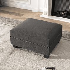 a gray ottoman sitting on top of a rug in front of a fire place with a remote control