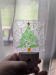 a hand holding a cell phone with a stained glass christmas tree on the front window