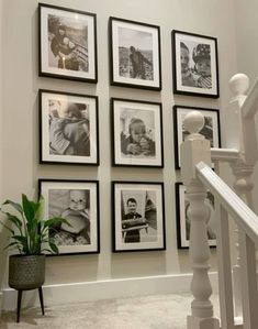 a bunch of pictures hanging on the wall next to a banister with a potted plant