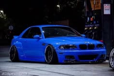 a blue car is parked in front of a gas pump at night with its lights on