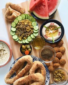 a wooden cutting board topped with different types of food and drinks next to watermelon slices