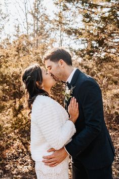 a bride and groom kissing in the woods