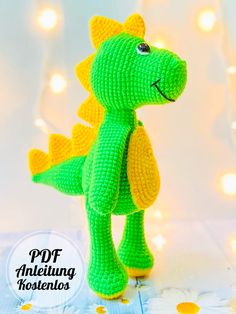 a crocheted green and yellow toy dinosaur on a wooden surface with lights in the background