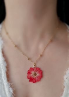 a close up of a person wearing a necklace with a red flower on the front