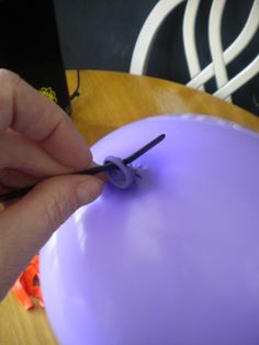 a person is cutting the end of a purple balloon with scissors on a wooden table