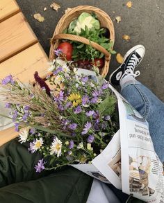 a basket filled with lots of flowers sitting on top of a wooden bench next to a person