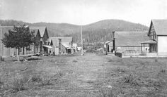 an old black and white photo of houses in the country side with mountains in the background