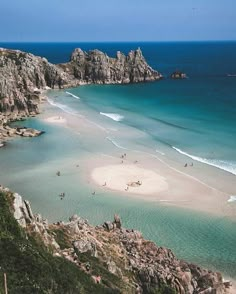 people are swimming in the ocean near some rocks and sand, while others swim in the water