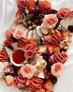 an arrangement of fruit and flowers on top of a white table cloth, with the center surrounded by other food items