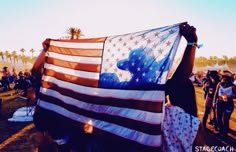 a person holding an american flag in their hands at a music festival with other people