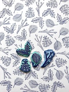 three blue flowers and leaves are on a white tablecloth with black ink drawings in the background