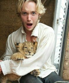 a man is holding a tiger cub in his arms while sitting on the ground with it's mouth open