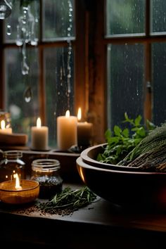 candles and herbs on a table in front of a window with rain drops falling down