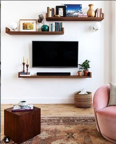 a living room with a tv and some shelves on the wall above it is a pink chair