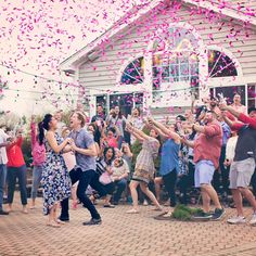 a group of people are throwing confetti into the air in front of a house