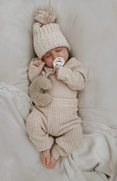 a baby in a knitted outfit sleeping on a blanket with a pacifier in its mouth