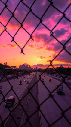 the sun is setting over an interstate with cars driving down it's lane in front of a cityscape