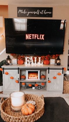 a television sitting on top of a tv stand next to a basket filled with pumpkins