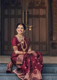 a woman sitting on the steps in front of a door wearing a red and gold sari