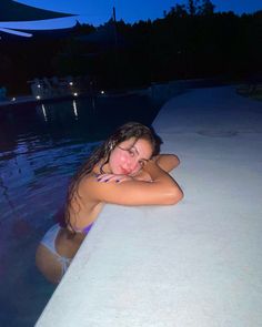 a woman in a bathing suit leaning on a wall next to the water at night