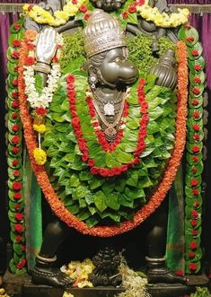 the statue is decorated with flowers and garlands on it's head, surrounded by greenery