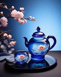 a blue tea pot and saucer sitting on top of a plate next to flowers