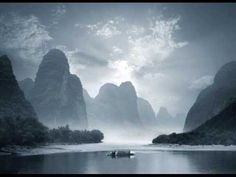 a boat floating on top of a body of water near tall mountains under a cloudy sky