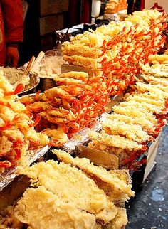 many different types of food are lined up on a long table with people in the background