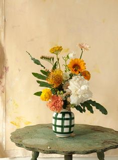 a vase filled with lots of flowers sitting on top of a wooden table next to a wall