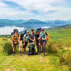 four people with backpacks and hiking poles standing on the side of a grassy hill