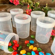 plastic cups filled with jelly beans on top of a wooden table next to red flowers