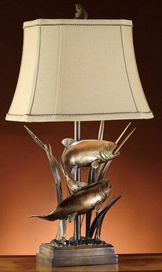 The striking Lake Marsh Table lamp is an elegant addition to your lakeside home. Measuring 32" tall, including shade, this rustic styled lamp features a typical marshland scene, cast in highly detailed resin, with a burnished bronze patina and wood finish that gives it the sophisticated look of cast bronze. Set of two lamps. The rectangular beige fabric shade is made of natural linen and measures 16" wide x 11" deep x 11" tall. 100 watt bulb max. This popular lamp is on backorder. Est. ship earl Fishing Themed Bedroom, Fish Lamps, Cave Lighting, Ranch Horse, Fishing Cabin, Industrial Lamps, Rustic Table Lamps, Cattle Ranch, Bronze Table Lamp