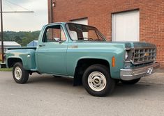 an old blue pickup truck parked in front of a brick building