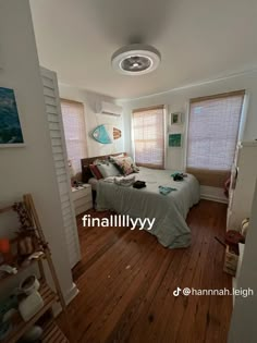 a bed room with a neatly made bed next to two windows and a wooden floor