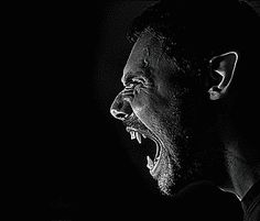 a man with his mouth wide open in the dark, screaming at something he is holding