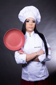 a woman holding a red frisbee in her right hand and wearing a chef's hat