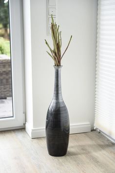 a black and white vase sitting on top of a wooden floor next to a window