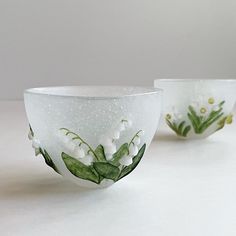 two glass bowls with white flowers and green leaves painted on the sides, one is empty