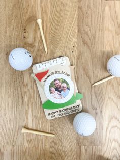 two golf balls and tees on a wooden table with a card for a father's day