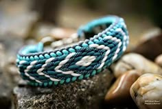 two blue and white bracelets sitting on top of a rock next to some seashells