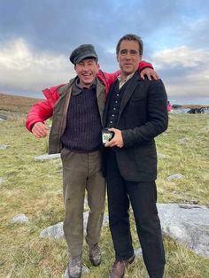 two men standing next to each other on top of a grass covered field with rocks