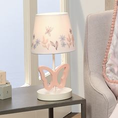 a pink lamp sitting on top of a table next to a white chair and window