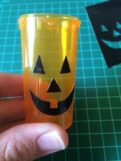 a hand holding an orange plastic cup with a jack - o'- lantern face on it