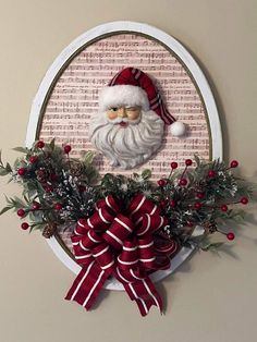 a santa clause is hanging on the wall above a wreath with holly and red ribbon